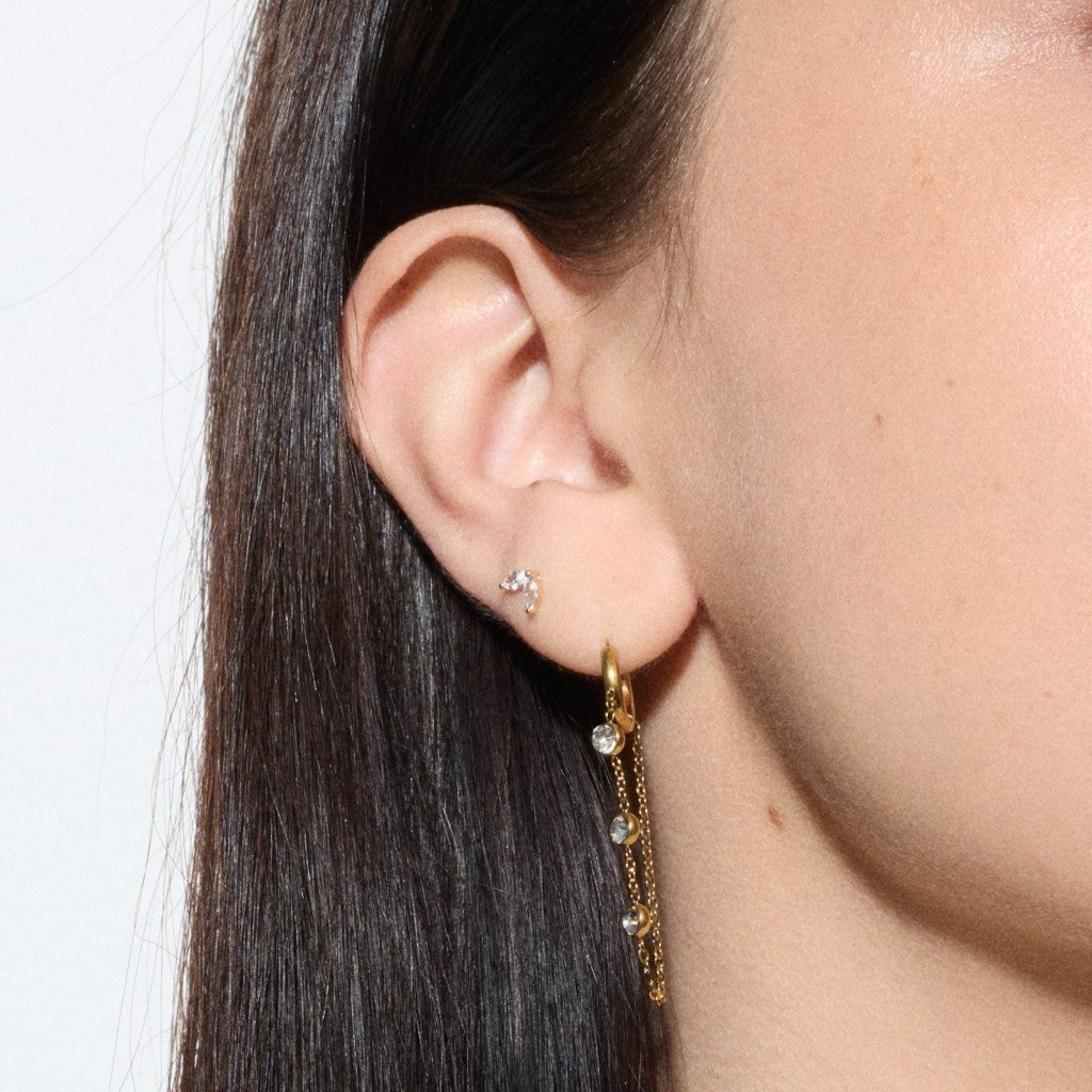 Close-up of ear wearing a gold chain dangle hoop earring with clear cubic zirconia accents and a matching gold crescent stud.