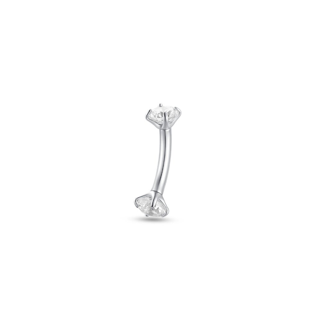 Close-up of an ear wearing a silver-tone titanium curved barbell with a round clear cubic zirconia in a claw setting, internally threaded, styled in the inner ear alongside gold hoops and a pavé cuff.