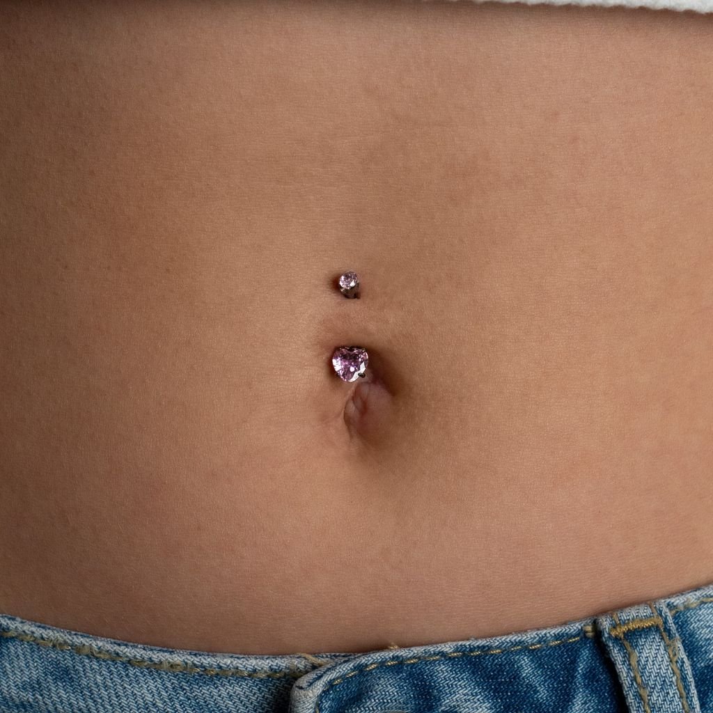 Titanium navel bar with heart-shaped pink cubic zirconia in a claw arc setting, shown worn in a navel piercing.