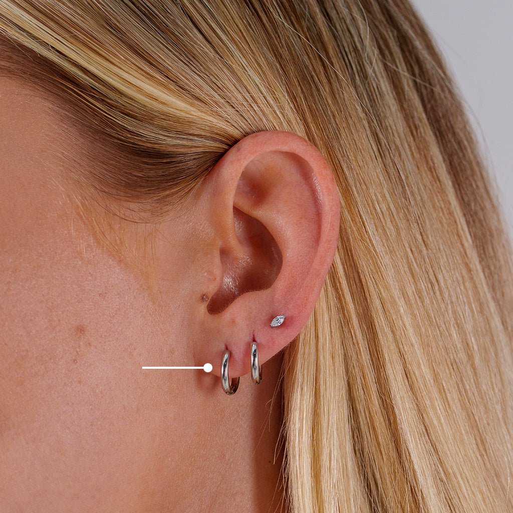 Close-up of a model’s ear wearing titanium classic bold hoop earrings in the lobe, shown in a smooth polished finish with a subtle size comparison between the hoops.