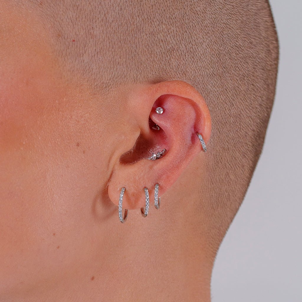 Titanium classic hoop earrings with clear cubic zirconia in silver tone, shown worn across multiple ear lobe piercings in a stacked ear styling