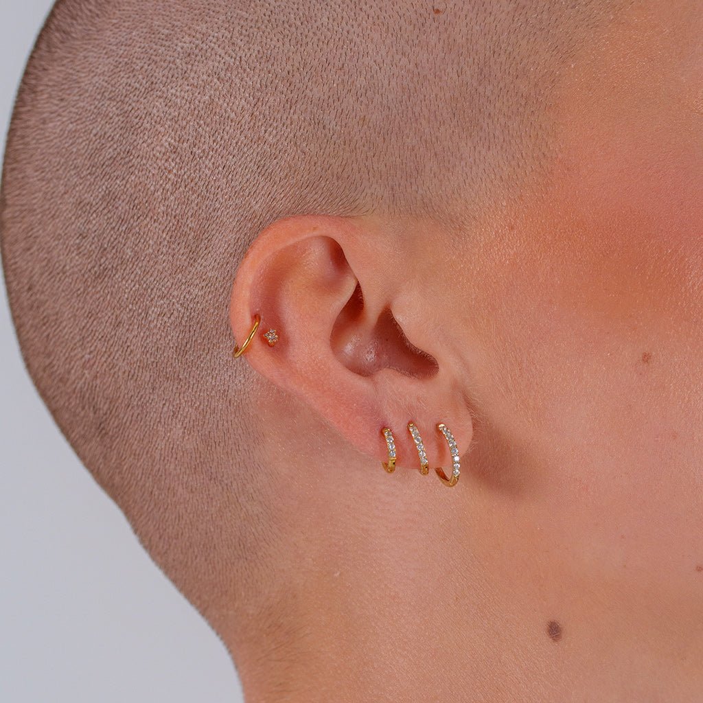 Titanium classic hoop earrings with clear cubic zirconia in gold tone, worn across multiple ear lobe piercings in a stacked ear styling