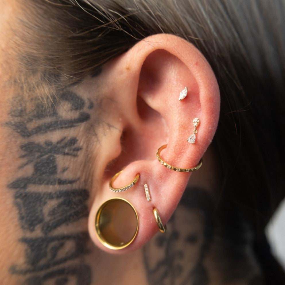 14K solid gold internally threaded piercing top with round clear cubic zirconia and pear-shaped cubic zirconia dangle worn in the ear