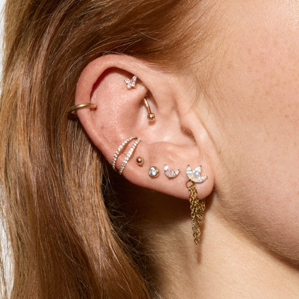 Close-up of ear styled with a gold helix hoop, rook curved barbell, double pavé ear cuff, butterfly chain stud and mixed cubic zirconia flatback earrings.