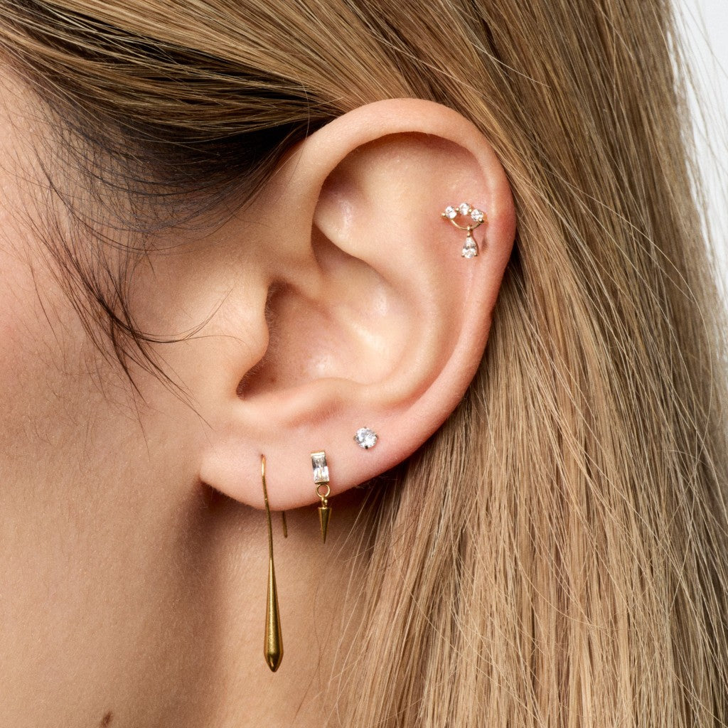 Close-up of ear with gold drop pendant earrings and 14K gold clear CZ triple claw dangle piercing top
