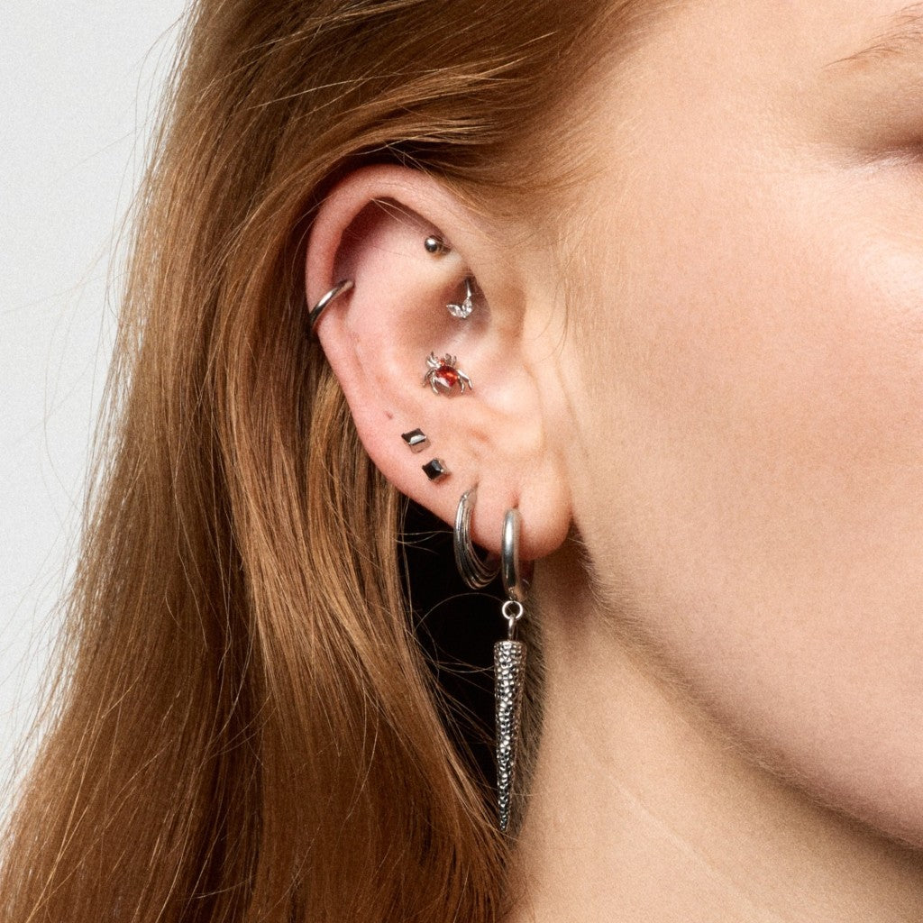 Close-up of ear with silver cone spike earrings and titanium red CZ spider piercing top
