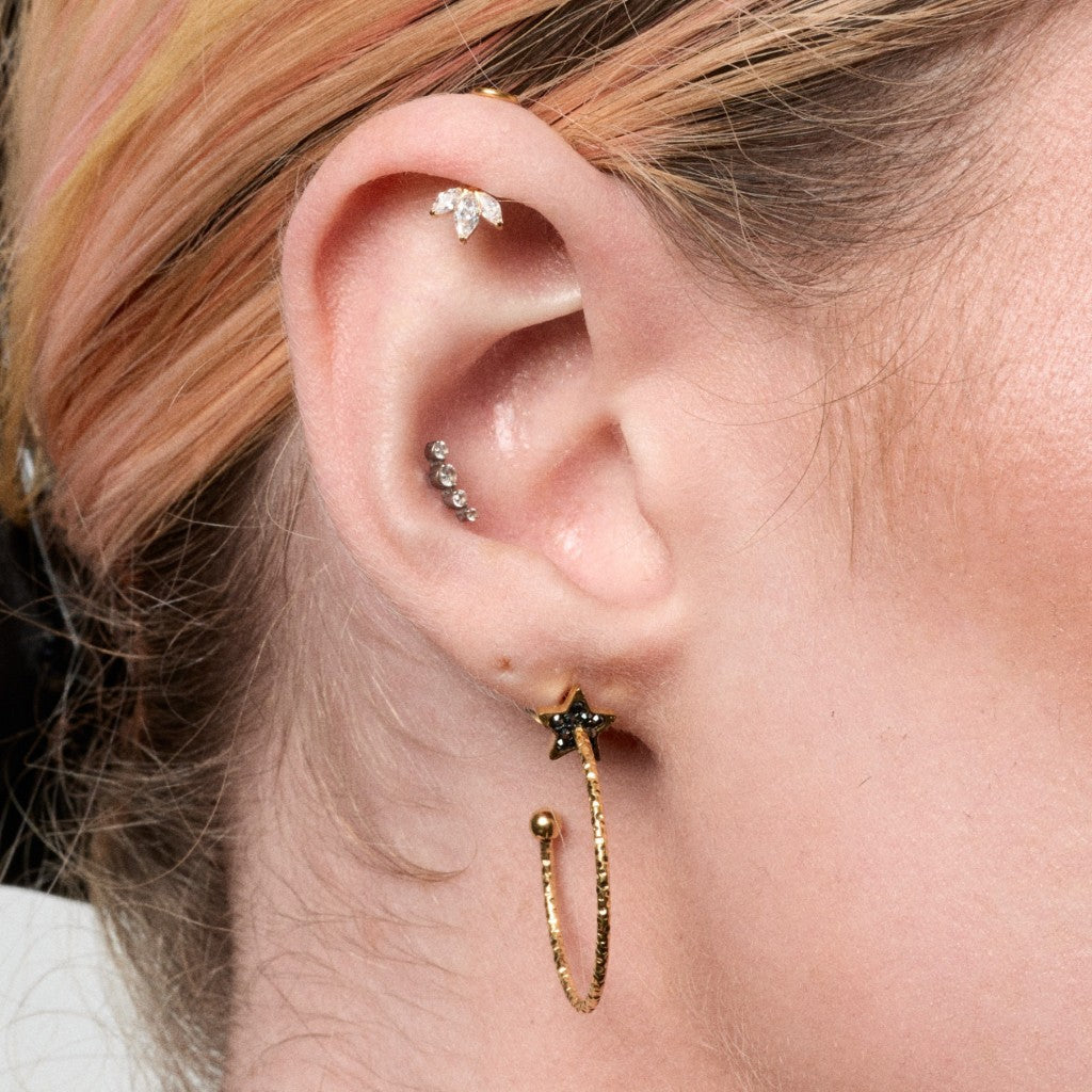 Close-up of ear with gold CZ three-marquise flatback, silver curved CZ piercing and gold black star hoop earring
