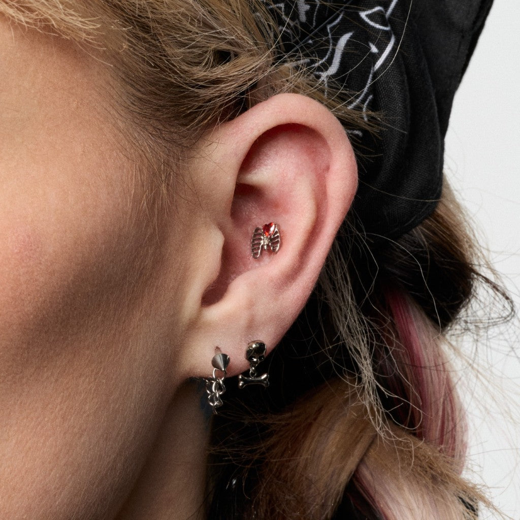 Close-up of ear with silver black skull dangle and silver red CZ cage heart flatback piercings
