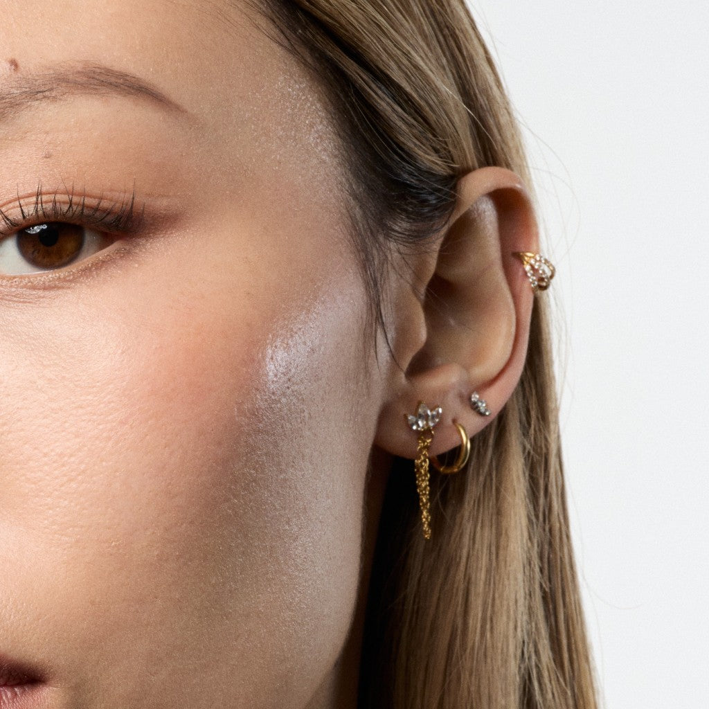 Close-up of a woman's ear wearing multiple gold and silver ear piercings, including hoop, cartilage, and lobe earrings, against a clean white background.
