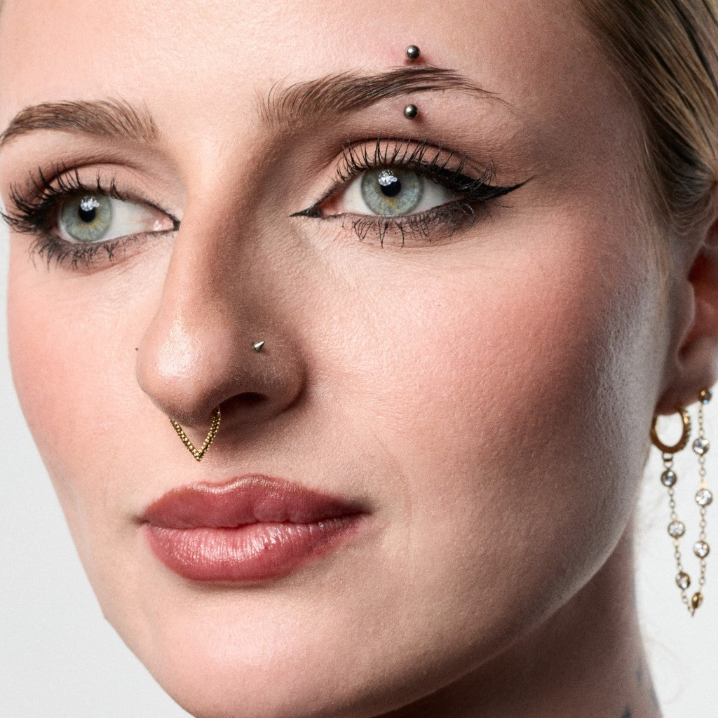 Close-up of model wearing a gold hammered V-shaped segment ring septum piercing
