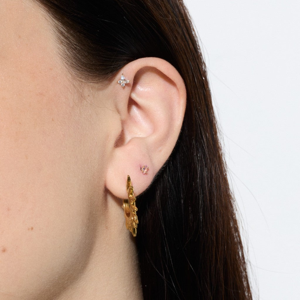 Close-up of ear featuring a clear cubic zirconia helix flatback, pink butterfly stud and gold sunburst hoop earring.