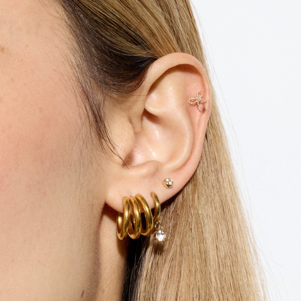 Close-up of ear styled with stacked gold hoop earrings, polished gold ball stud, bow helix flatback and a clear cubic zirconia dangle hoop.