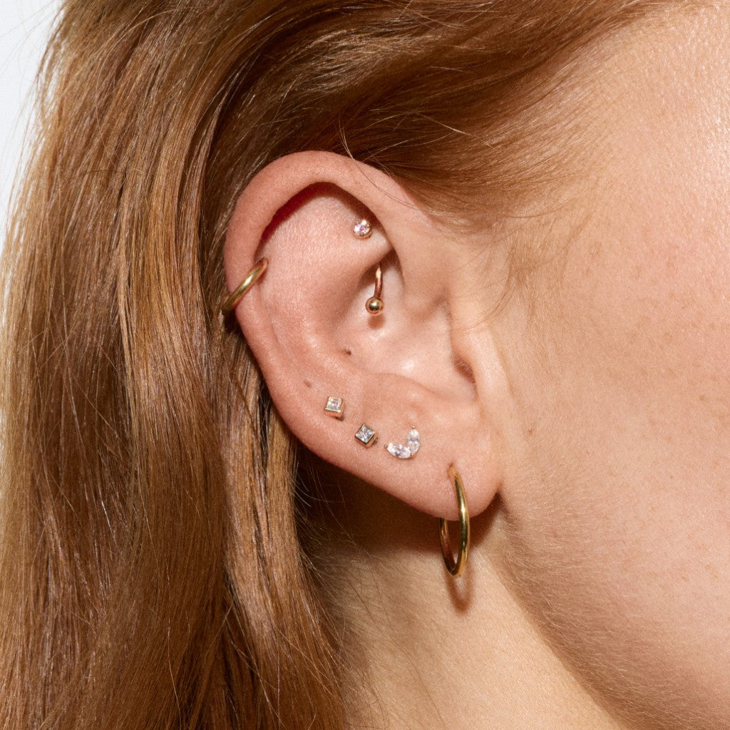 Close-up of ear styled with gold helix hoop, rook curved barbell, gold hoop earring and mixed cubic zirconia flatback studs.