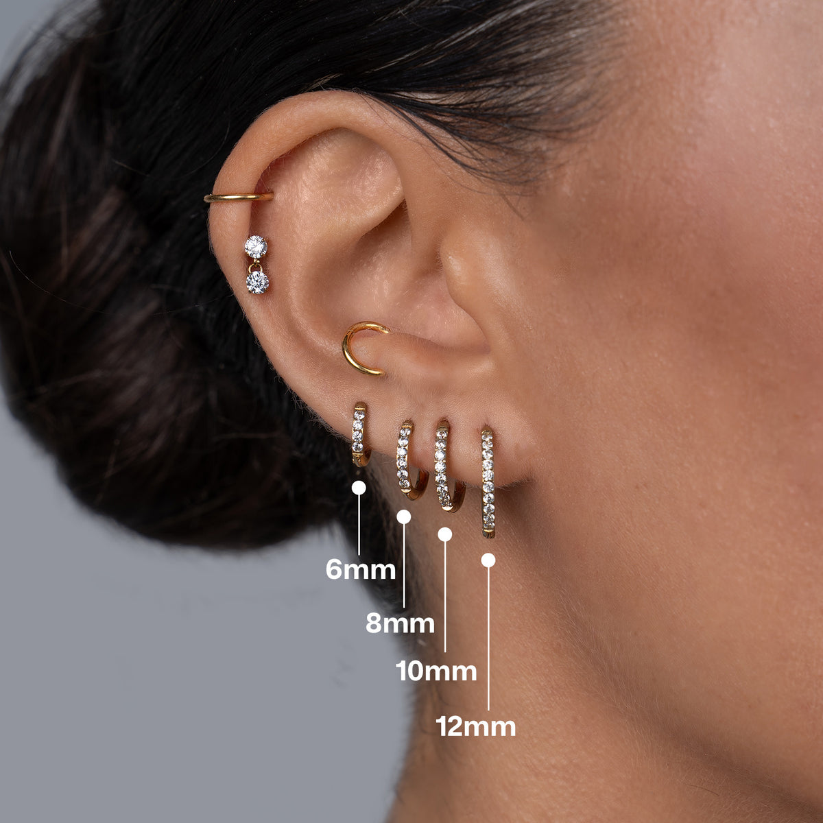 Titanium classic hoop earrings with clear cubic zirconia in gold tone, shown in graduated sizes 6mm, 8mm, 10mm and 12mm worn across multiple ear lobe piercings for a stacked look