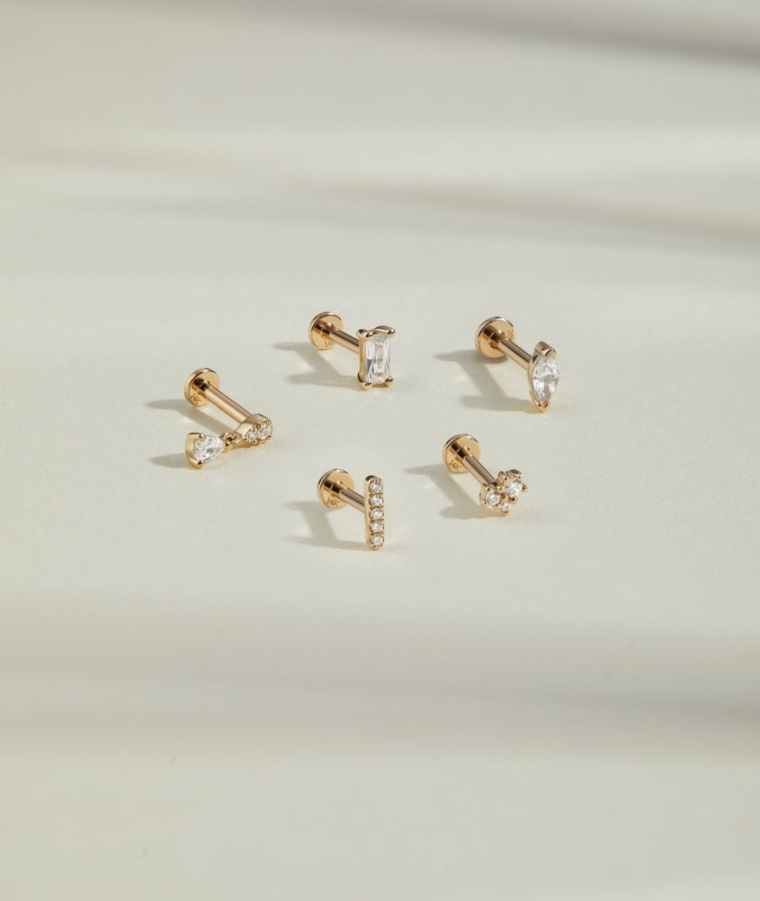 Set of gold earrings with clear gemstones on a light beige background