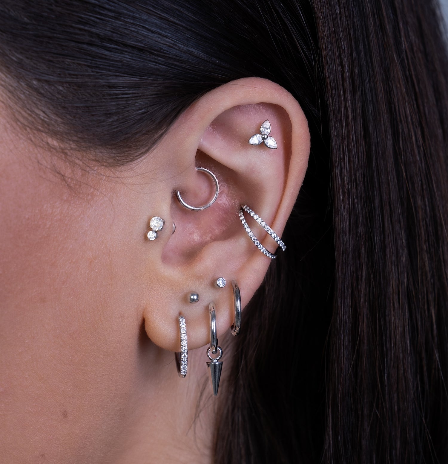 Close-up of an ear with multiple silver earrings against a dark background