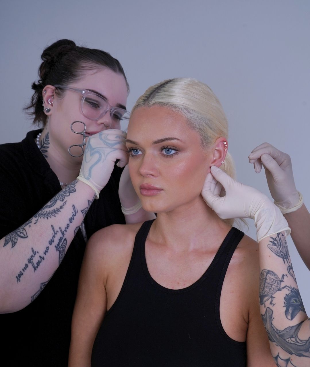 Person doing piercing to another person's face against a plain background